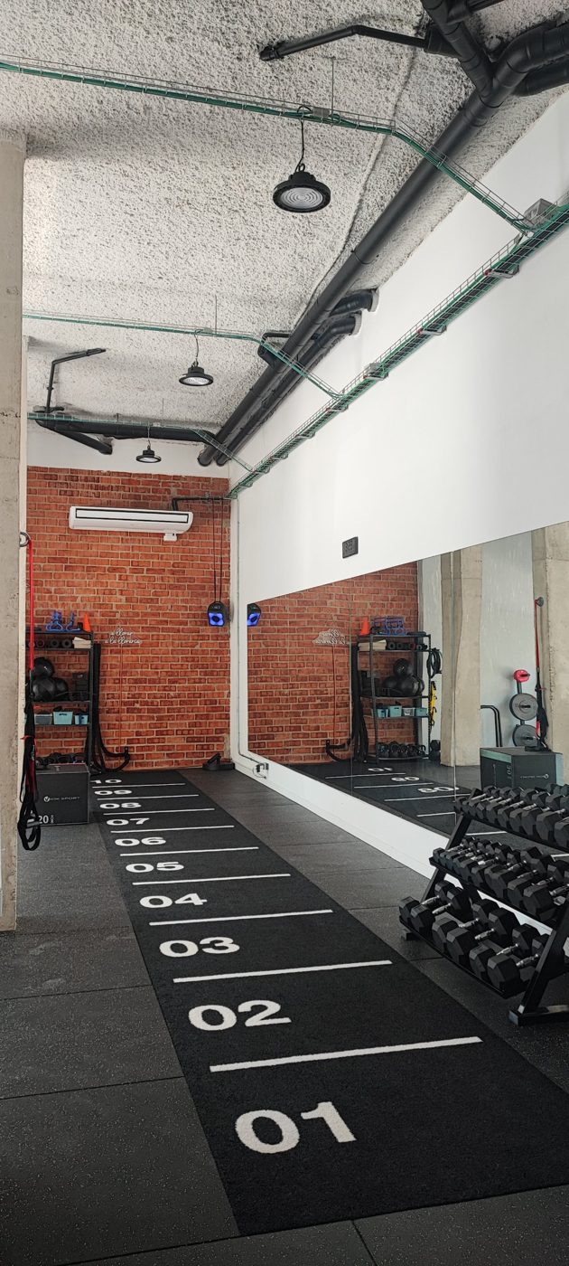 Sala de entrenamiento con pista de carrera numerada, mancuernas, suspensión y espejo