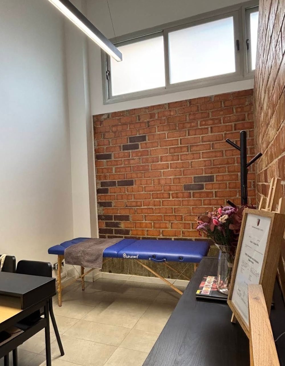 Sala de fisioterapia con camilla, pared de ladrillo y luz natural